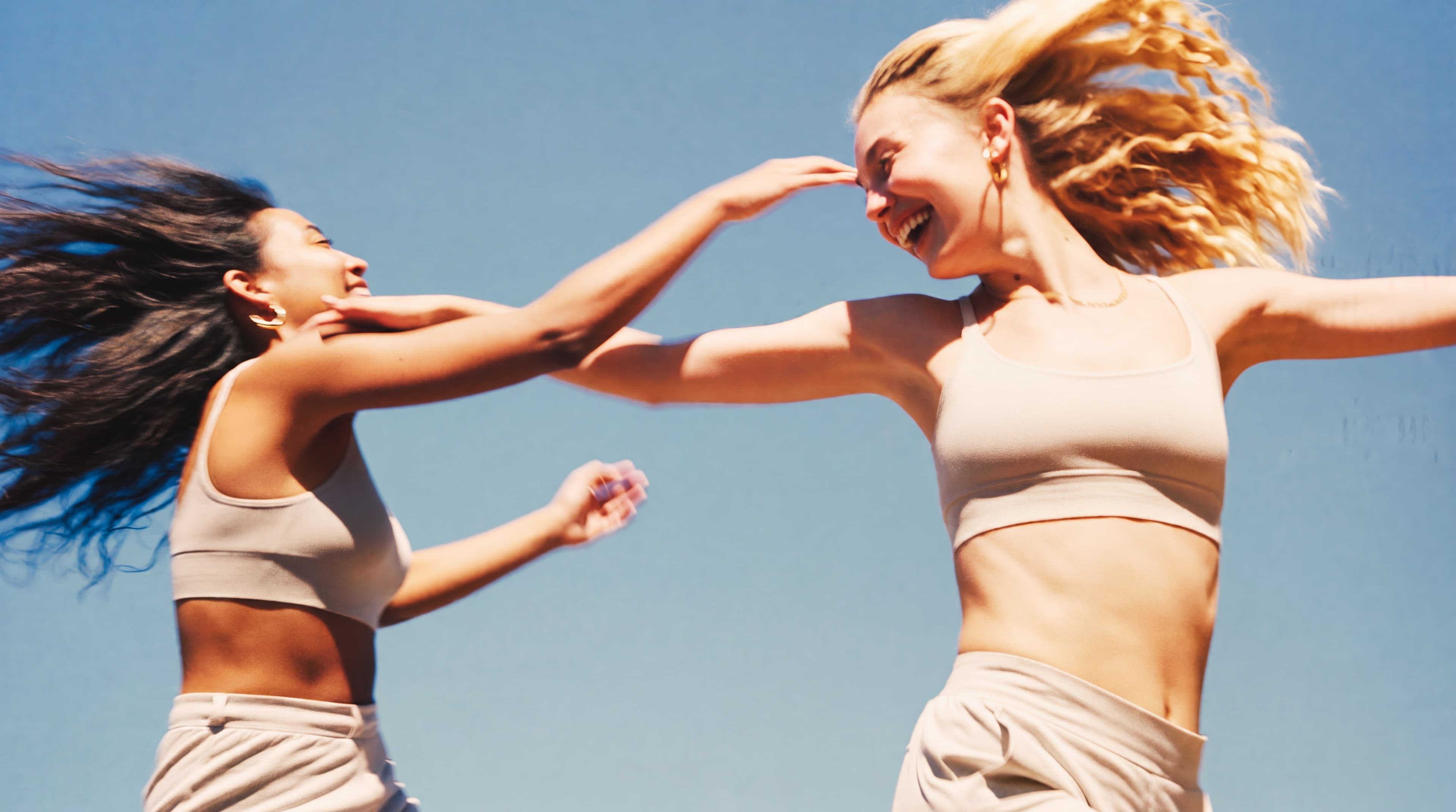 Two friends laughing together mid-jump under a clear blue sky