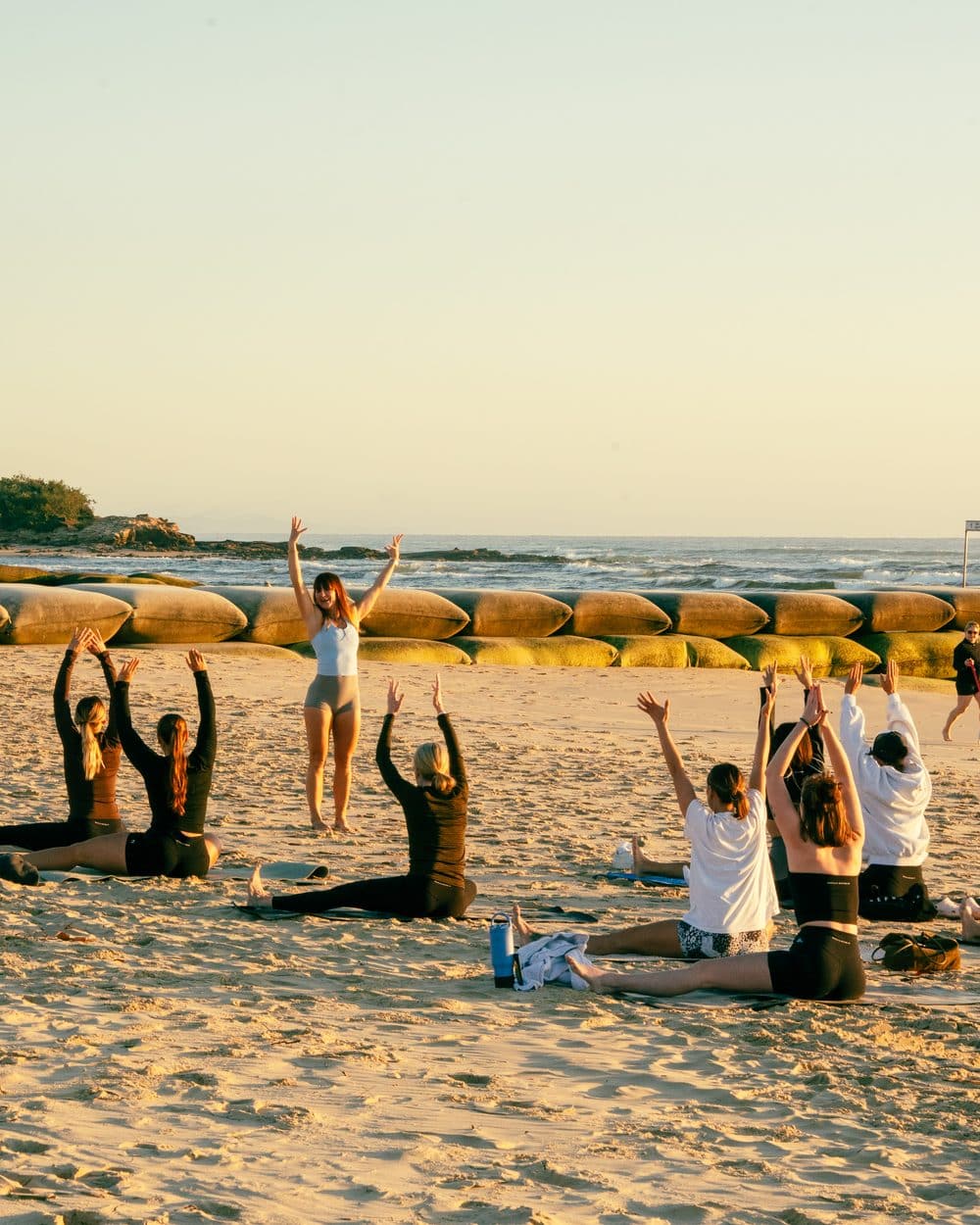 Sunrise Yoga Flow on the beach at dawn, a row of people reaching up with the sea behind.